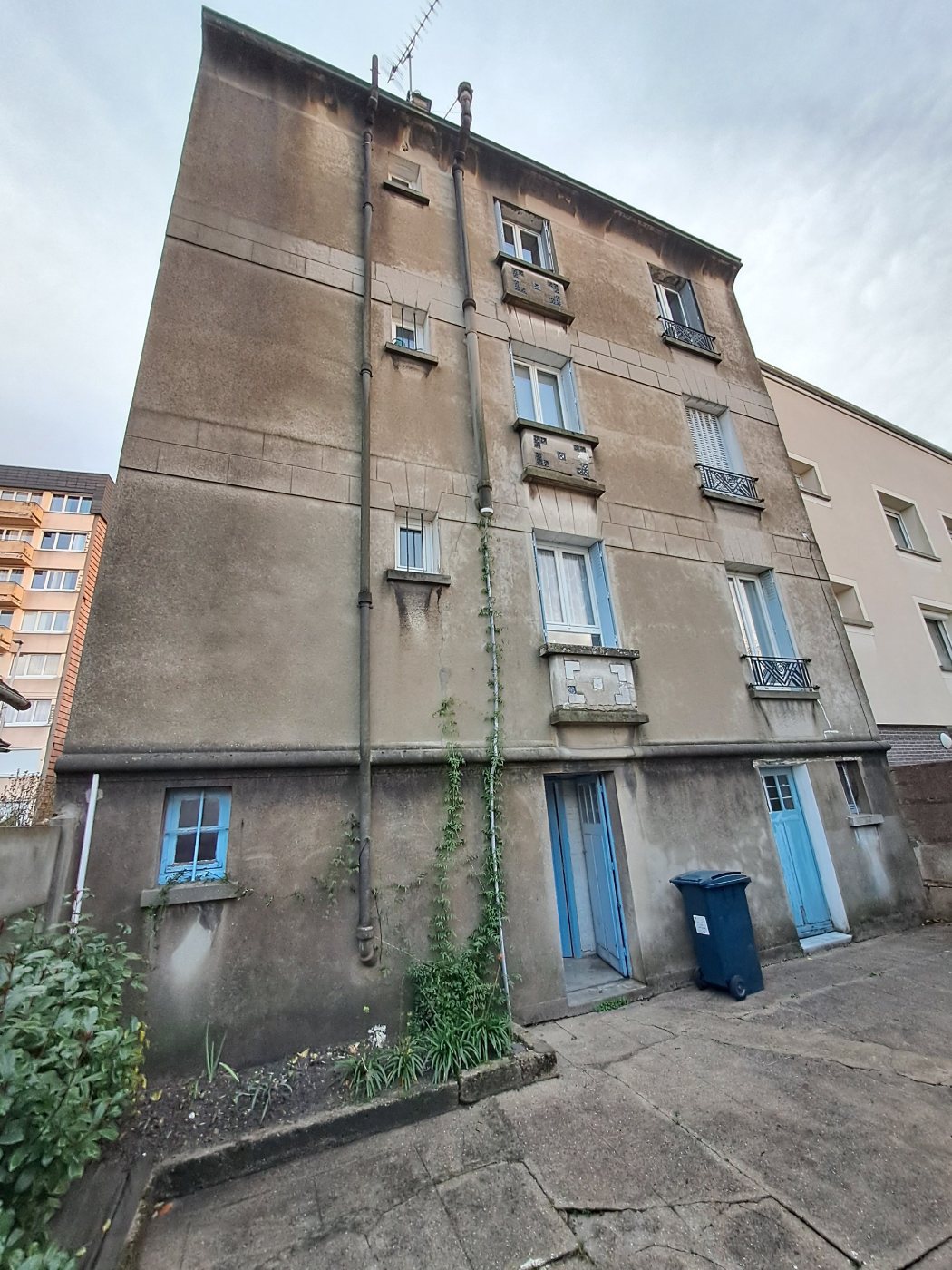 Façade arrière de la copropriété avant travaux : coulures, salissures, modénatures dégradées et végétation grimpante