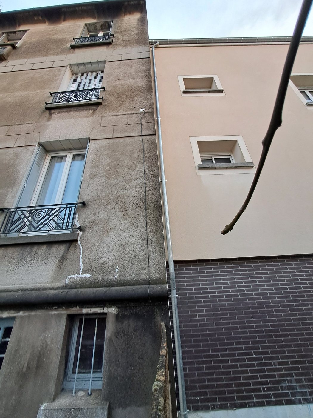 Détail de la façade avant travaux : fissure traversante sous une fenêtre repérée en blanc, à côté de l’immeuble voisin récemment ravalé