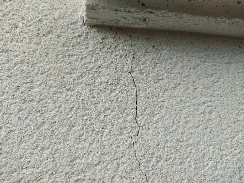 Gros plan d’une fissure dans l’enduit de façade partant de l’appui de fenêtre, fissure non structurelle limitée à l’enduit