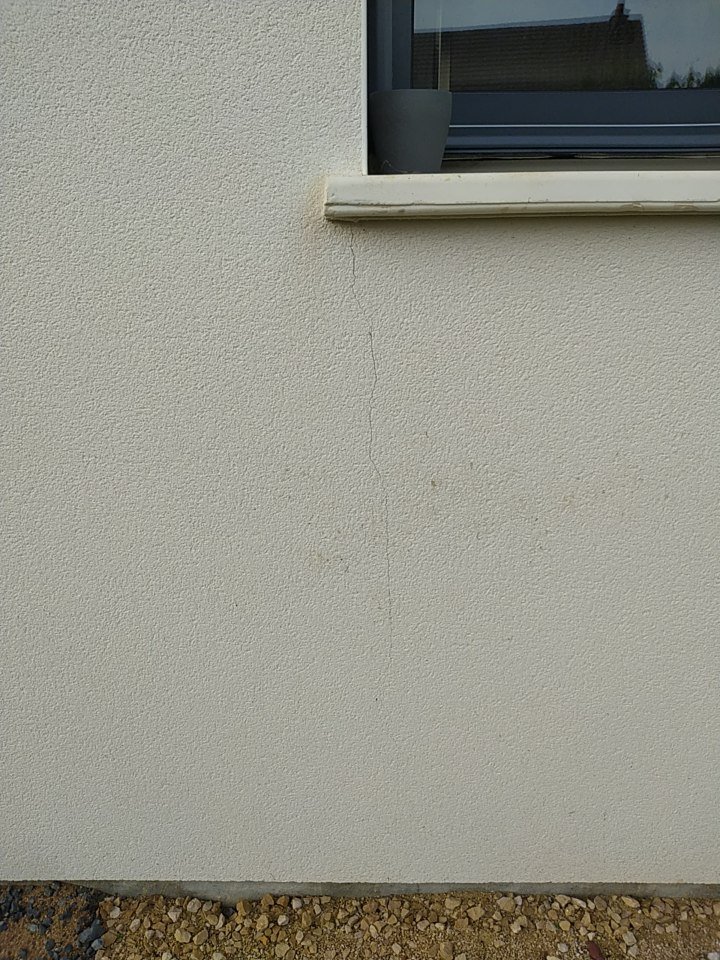 Fissure verticale dans l’enduit sous l’angle d’un appui de fenêtre, due à la dilatation ou à un décollement de l’enduit