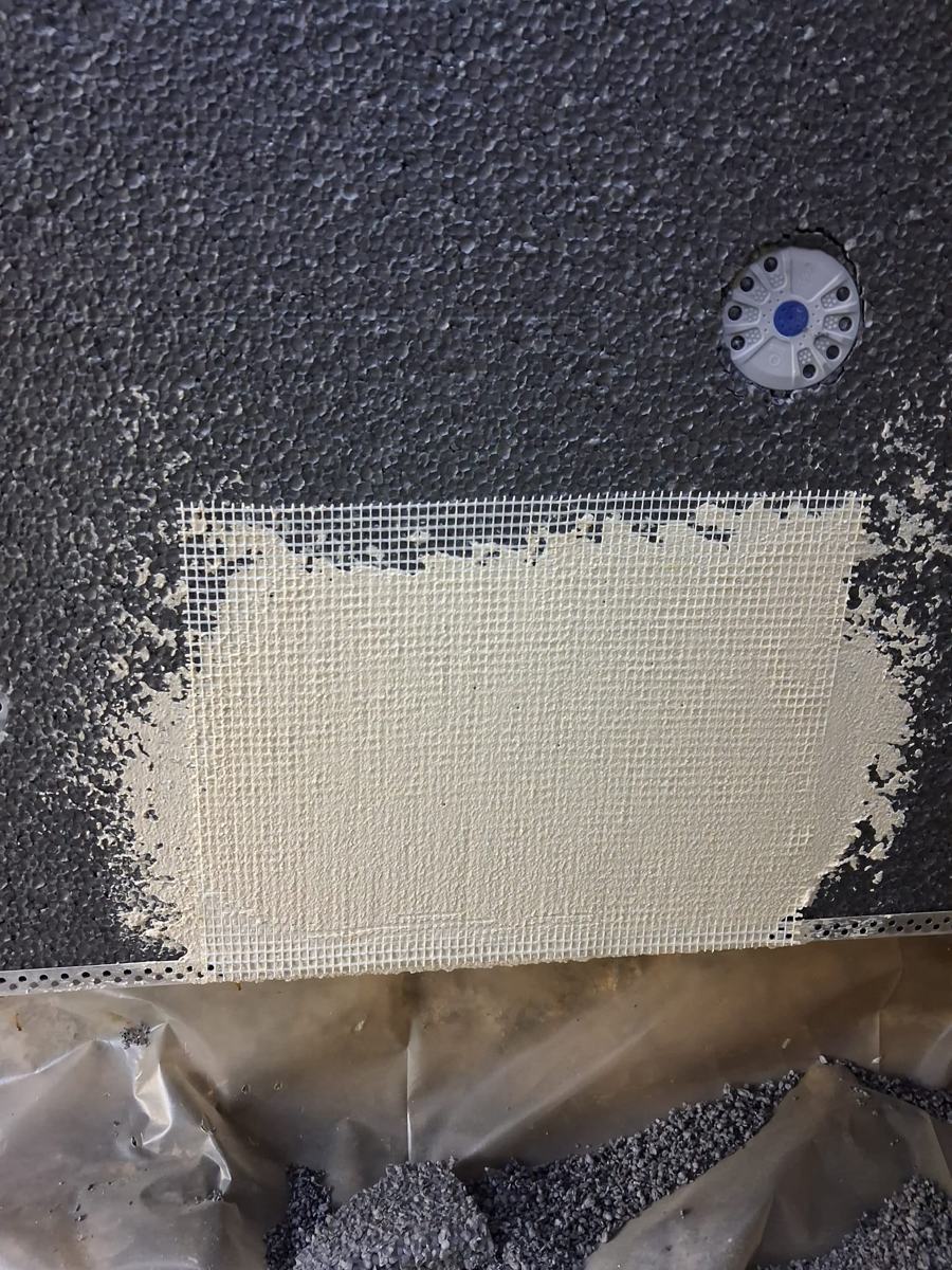 Bande d'armature en fibre de verre noyée dans le sous-enduit à la jonction de deux profilés de départ, sur PSE gris