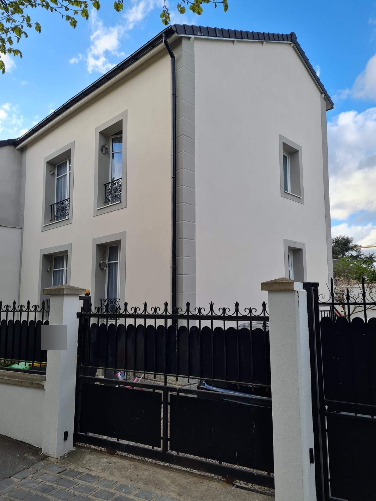 Pignon d'une maison au Perreux-sur-Marne après isolation par l'extérieur : chaînes d'angle et encadrements en modénatures talochées grises sur enduit gratté clair