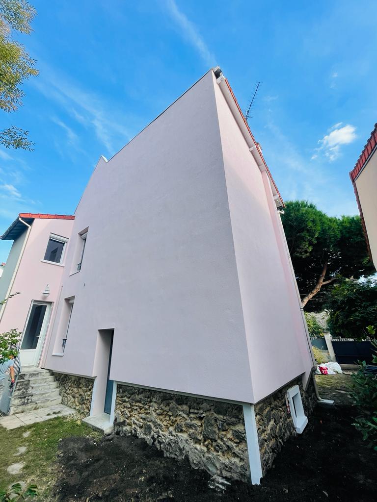 Façade arrière et pignon d'une maison à Nogent-sur-Marne après isolation par l'extérieur en laine de roche : enduit rose lisse au-dessus du soubassement en meulière